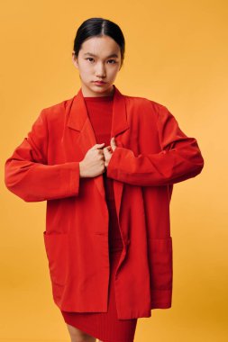 Sarı arka planda duran kırmızı ceketli ve uyumlu elbiseli genç kadın modelin portresi. Modern moda görünüş, keskin minimalist stüdyo ortamında temiz stil..