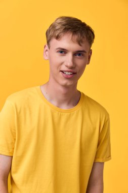 Sarı tişörtlü gülümseyen genç adam parlak sarı bir arka plan, günlük tarz, stüdyo düzeneği, çağdaş yaşam tarzı, moda veya teknoloji teması için ideal.