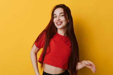 Sarı duvarın yanında duran uzun düz saçlı, kırmızı bluzlu, gülümseyen kadın. Genç manken, gündelik kıyafet ve modern güzellik ve kişisel fotoğraf için mutlu ruh hali..