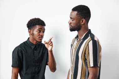 Esmer tenli Afro-Amerikalı erkekler önemli bir şeyi tartışıyor. Siyah gömlekli bir adam el hareketleriyle açıklarken diğeri çizgili gömlekli olan dikkatle dinliyor..