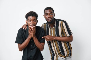 Koyu tenli genç siyahi erkekler şok ve neşe ifade ediyor. Birinin yüzünde elleri, diğerinde ise beyaz arka planda günlük gömlekler giyiyor..