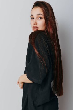 Yan duran siyah tişörtlü, uzun düz saçlı genç bir kadının portresi. Tarafsız arka plan, moda ve doğal görünümlü güzellik kavramında ciddi bir ifadeye sahip kadın pozu.