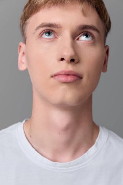 Yukarı bakan genç bir erkek, temiz ten, yumuşak gölgeler, basit kıyafetler, sakin tavır, ruh hali, arzu ve bir stüdyo ortamındaki iç gözlem üzerine odaklan.