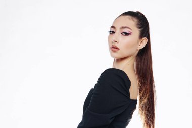 Şık bir bayan model, zarif siyah giysiler içinde keskin pembe göz farı ve parlak uzun saçlar sergiliyor. Temiz beyaz bg ile modern güzellik ve moda konsepti.