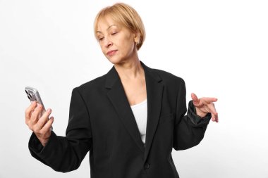 Siyah blazer ceket giymiş olgun bir kadın diğer eliyle akıllı telefona bakar. Beyaz arka planda izole edilmiş, teknoloji kullanımı, iletişim ve iş dünyası kavramı.