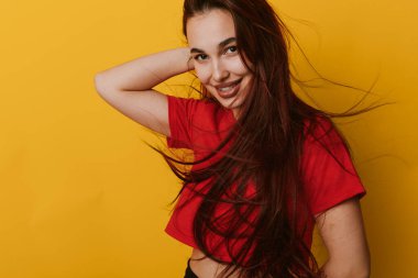 Gülümseyen, dalgalı saçlı, kırmızı bluzlu, parlak sarı arka planda poz veren genç bir kadın. Kendine güvenen bir kadın portresi ve moda veya yaşam tarzı konsepti için rahat bir poz..