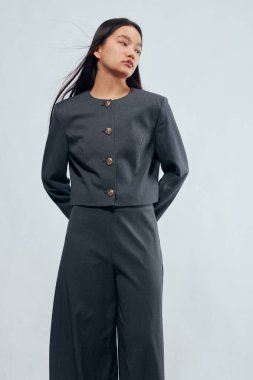 Gri takım elbiseli genç kadın elleri arkada duruyor. Şık kıyafetler, günlük iş kıyafetleri, moda portresi ve temiz bir geçmişi ve doğal görünüşü olan modern tarz..