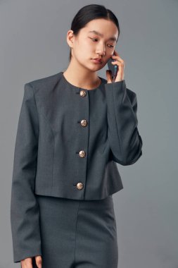 Gri takım elbiseli bir kadın işçi telefon görüşmesi için akıllı telefonu kullanıyor. Şirket iletişimi için sade arka planda düzgün saç stili olan ofis kıyafetli genç profesyonel bir kadın..