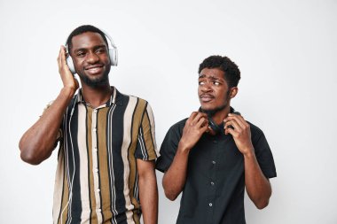 Siyah derili genç Afrikalı erkekler kulaklık takıyor, beyaz arka planda duruyorlar, biri çizgili gömlekle gülümsüyor, diğeri siyah kulaklık takıyor..