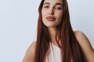 Düz kızıl saçlı ve kameraya bakan zarif makyajlı genç bir kadın portresi. Açık tenli ve minimalist fotoğrafçılıkta beyaz zemin üzerinde rahat durabilen kadın modeli.