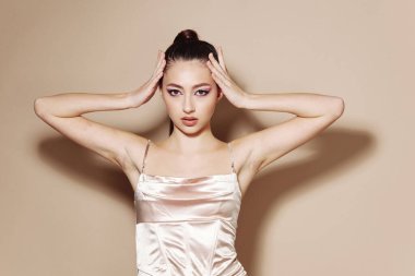 Moda mankeni, stüdyo ortamında parlak saten bir elbise giyerken pürüzsüz cilt bakımı ve makyaj yapar. Tarz, moda ve sağlık temalarını vurgulayan yaratıcı güzellik portresi.