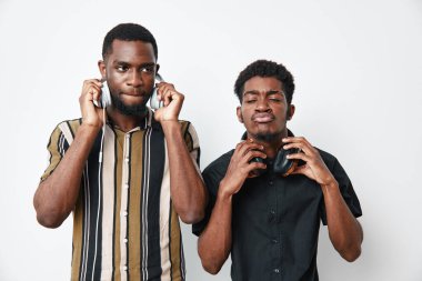 Kulaklıkları ayarlayan koyu tenli iki Afrikalı adamın portresi. Biri çizgili gömlek, diğeri siyah gömlek giyiyor, beyaz arka planda dışlanmış, anlamlı yüzler..
