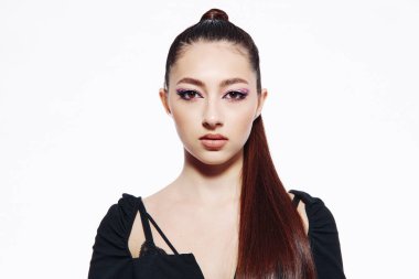 Özel bir saç stili ve kalın göz estetiği olan, son moda, omuz dışı giysiler giyen bir kadın modelin yakın çekimi. Yüksek moda ve yaratıcı güzellik bağlamında stüdyo çekimi.