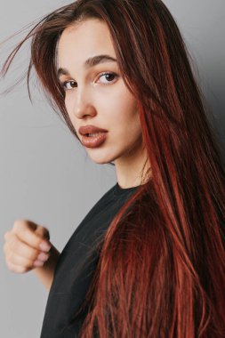 Kızıl saçlı, siyah bluzlu ve kameraya bakan genç bir kadının portresi. Doğal güzellik, pürüzsüz bir ten ve rahat bir poz. Gri arka planda, yakın planda..