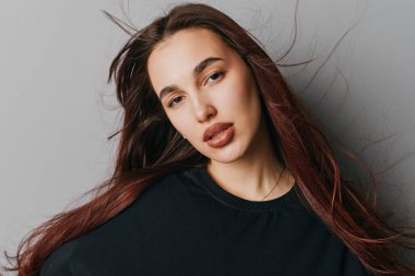 Kameraya bakan kızıl saçlı ve nötr makyajlı genç bir kadının portresi. Siyah gömlekli, doğal görünümlü ve arka planda hafif ışıklandırmalı bir kadın model..