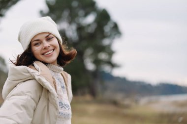 Açık hava kış portresi gülümseyen palto beresi, neşeli bir kadının portresi, soğuk bir günün tadını çıkaran, rahat bir poz, sıcak bir ceket ve örgü şapka, rahatlık, sağIık ve kış mutluluğu.