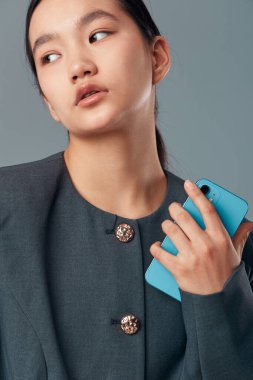 Koyu renk elbiseli zarif bir kadın elinde akıllı bir aletle kameradan dışarı bakıyor. Açık tenli, minimalist tarzda ve profesyonel portre ortamında düzgün saçlı bir kadın..