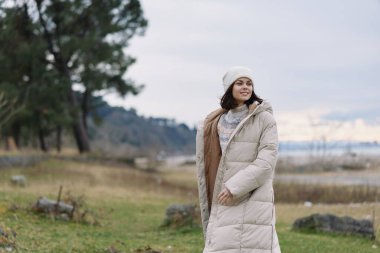 Kışlık kadın paltosu manzara göl manzarası serin günlük moda, göl kenarında şık bir şahsiyet, yumuşak ışık ve geniş ufuk rahatlığı, sıcaklığı ve mevsimsel gardırobu vurguluyor.