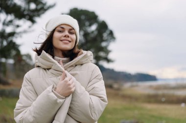 Açık havada, kışın gülümseyen bir kadının portresi, sıcacık bir palto, bere ve doğal bir eşarp ile soğuğu kucaklıyor..