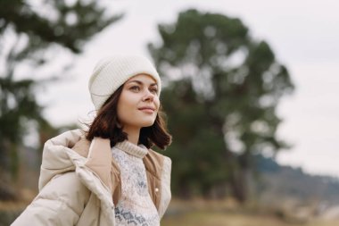 Kışlık ceketli ve bereli bir kadın, sakin doğa ve nazik rüzgar yakalayan bir portre, vurgu tarzı, konfor ve açık hava modası..