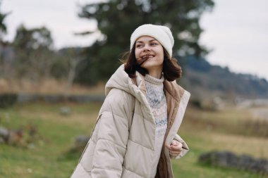 Açık kırsalda, sıcak giyimli bir kadın. Yumuşak gün ışığı, rahat bir duruş ve nazik bir ruh hali. Doğa aşıkları ve açık hava modası için mükemmel..