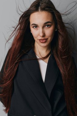 Genç bir kadının portresi dalgalı saçlar ve siyah ceket ve beyaz gömlek giymiş hafif bir gülümseme. Kapalı alanda, arka planda ve doğrudan göz teması kurarak poz veriyor..