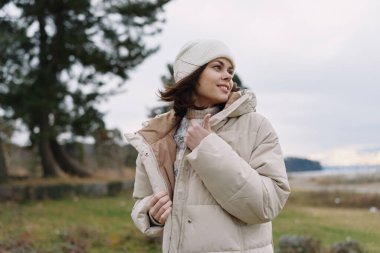 Soğuk bir manzarada kalın bir kabarık ceket ve bere giyen bir kadının açık hava portresi, serinlik, tarz ve sükunet yakalamış..