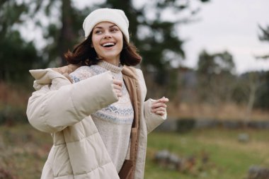 Kışlık ceketli ve bereli bir kadının açık hava portresi, eşarp, sıcak giysiler ve açık alanda rahat bir ruh haliyle gülümsüyor, mevsimlik tarzı ve konforu vurguluyor..