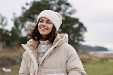 Sıcak bir palto ve bereyle gülümseyen bir kadının sıradan portresi. Açık hava manzarası, hafif bir esinti, doğal bir ışık ve dingin bir doğa ortamında neşeli bir ruh hali..