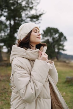 Açık havada sıcak kıyafetler giyen bir kadının portresi, serin havalarda konfor, moda ve doğal ışığı yakalıyor.