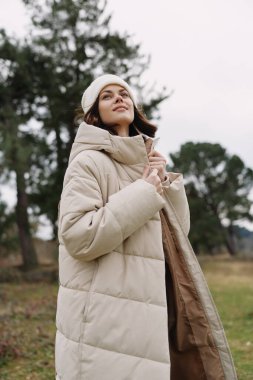 Açık havada palto giymiş, ağaçların ve açık arazinin ortasında soğuk hava titreşimlerini kucaklayan rahat, stil ve açık havada yaşayan bir kadının sıradan portresi..