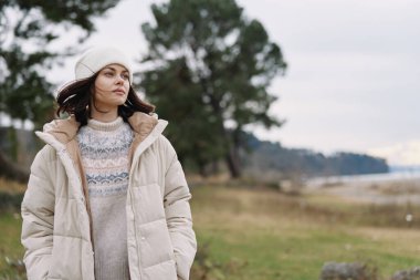 Sıcak bir palto giyen, deniz kenarında örgü ören, mevsimlik tarzını, serin esintiyi ve doğal manzarayı yakalayan bir kadının açık hava portresi..