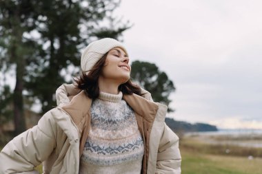 Rahat, rahat bir kadın portresi. Sıcak bir kazak ve bereyle serin havanın tadını çıkarıyor. Temiz havayı ve açık manzarayı kucaklıyor.