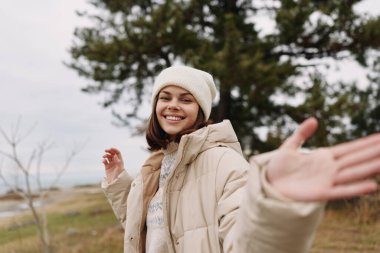 Sıcak bir palto ve bereyle gülümseyen kadın, kollarını dışarı uzatır, kış doğasının ve geniş manzaranın tadını çıkarır, rahat, kaygısız bir anda.