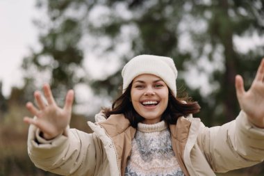 Açık hava kış sahnesinde neşeli bir kadın, sıcak bir palto ve örgü bir şapka, açık kollar ve parlak bir gülümseme mutluluk, rahatlık ve neşeli bir ruh hali içinde mevsimsel bir anda