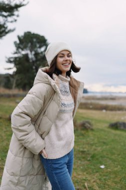 Açık havada kabarık bir ceket giyen, kazak ören ve bereli bir kadının doğal ışık ve güzel manzaralı bir parkta temiz havanın tadını çıkaran bir portresi..