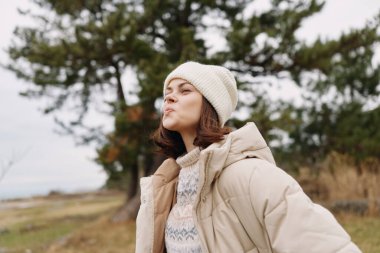 Kabarık bir palto giyen ve rüzgarlı bir açık havada çimen ve ağaçlarla örgü ören bir kadının portresi. Soğuk koşullarda sıcaklığı, tarzı ve dayanıklılığı aktaran sakin ve samimi bir sahne.