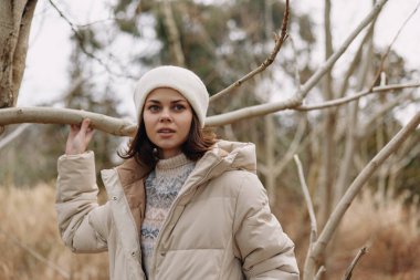 Kışın ağaçlarla çevrili, kalın palto ve bereli bir kadının açık hava portresi, soğuk hava ve kırsal doğal ortamda sakinlik, stil ve direnç taşıyor..