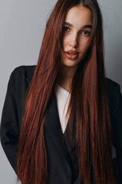 Gri duvarın önünde duran uzun kırmızı saçlı ve siyah ceketli kadın model. Yakın plan portre, stil, zarafet ve doğal görünüş, pürüzsüz cilt ve ciddi iç mekan fotoşopu..