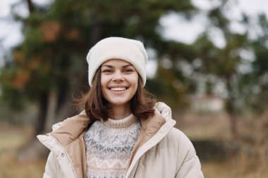 Paltosu ve örgü şapkası olan neşeli bir kadının portresi. Yumuşak doğal ışık. Park ortamında rahat moda..