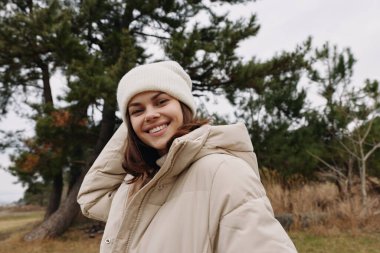 Rahat kabarık ceketli ve örgü şapkalı neşeli bir kadının portresi. Parka benzer bir manzarada temiz havanın tadını çıkarıyor. Rahatlamış bir ruh hali ve mevsimlik giysiler..