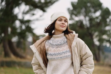 Temiz hava ve doğal çevreyle sakin bir kış sahnesinde örgü kazak ve bere giyen şık bir kadının portresi..