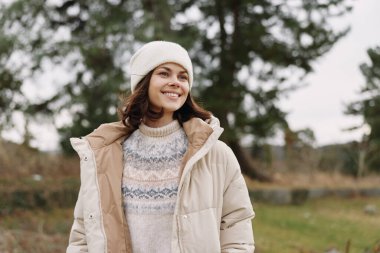 Açık havada pofuduk bir ceket giyen, kazak ve şapka ören, temiz havanın ve rahat sokak modasının ve mevsimsel rahatlığın tadını çıkaran bir kadının portresi.