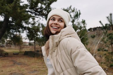 Açık hava kış ceketi, gülümseyen park portresi, güneşli bir park ortamında soğuk hava ve rahat bej kıyafetler, çağdaş moda ve açık hava giyimi için samimi bir yaşam tarzı..