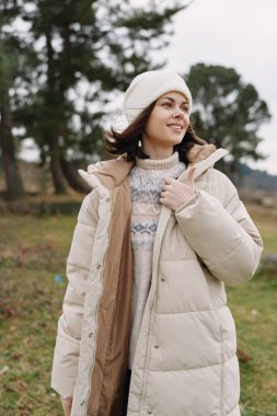 Açık havada, ağaçların arasında, sıcacık giyinen, rahat bir şekilde ışıldayan ve sakin bir sezon sahnesinde kendine güvenen bir kadının resmedildiği sıradan bir kış portresi..