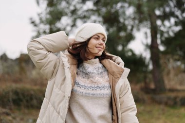 Donuk hava ve yumuşak doğal ışıkla parkta dikilen örgü kazak ve bere giyen bir kadının sıradan portresi sakin bir kış havasını yakalıyor..