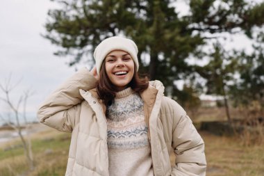 Kış kıyafetleri içinde neşeli bir kadının sıradan portresi, sıcacık ve rahat, doğal bir ortamda, rüzgarlı saçlar, sakin arka plan, gösterişli konfor, moda ve açık hava yaşam tarzı.