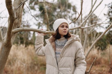 Açık hava portresi, kalın bir palto ve bere giyen, sakin bir kış ortamında sessiz kahverengi ve yumuşak bir ışıkla mesafeye bakan bir kadın..