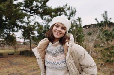 Serin bir parkta rahat bir bej ceket ve desenli bir süveter giyen mutlu kadın, rahat, doğal bir hayat tarzı portresi sunuyor..