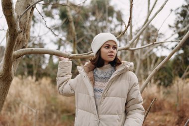 Açık hava portresi, kalın bir palto giyen ve çıplak dalların arasında örgü ören bir kadın, sakin bir kış havasını doğal bir orman ortamında yakalıyor..